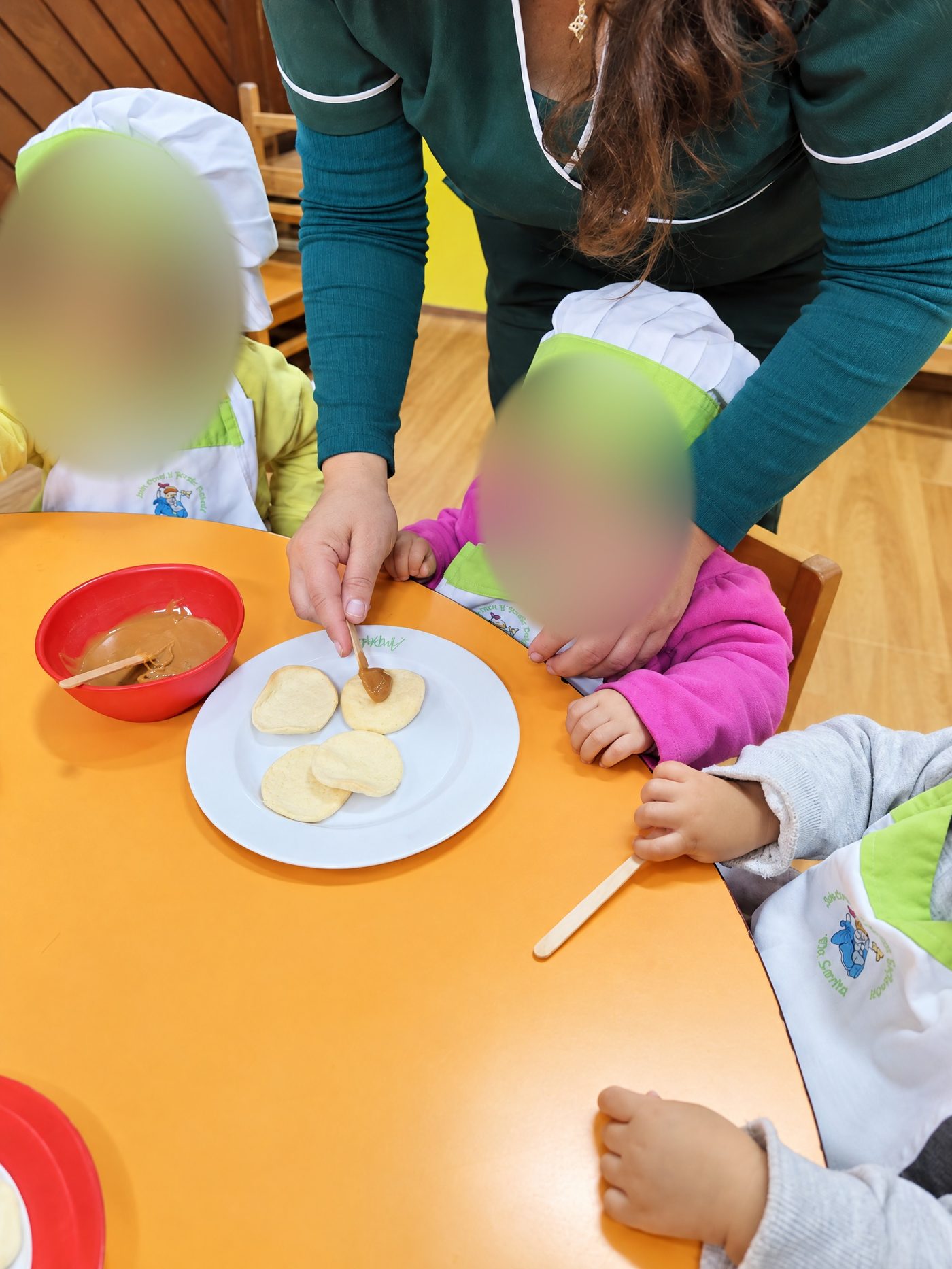 Niños pequeños con gorro de chef preparan galletas con ayuda de una tía