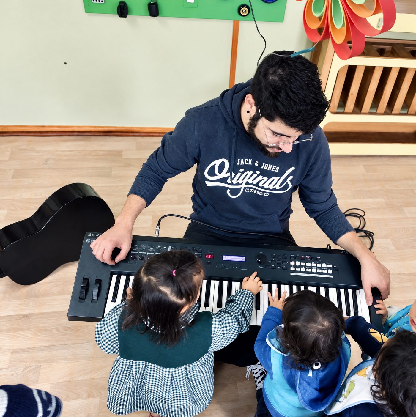 El profesor de música toca el teclado con niños y niñas del jardín, que aparecen de espaldas