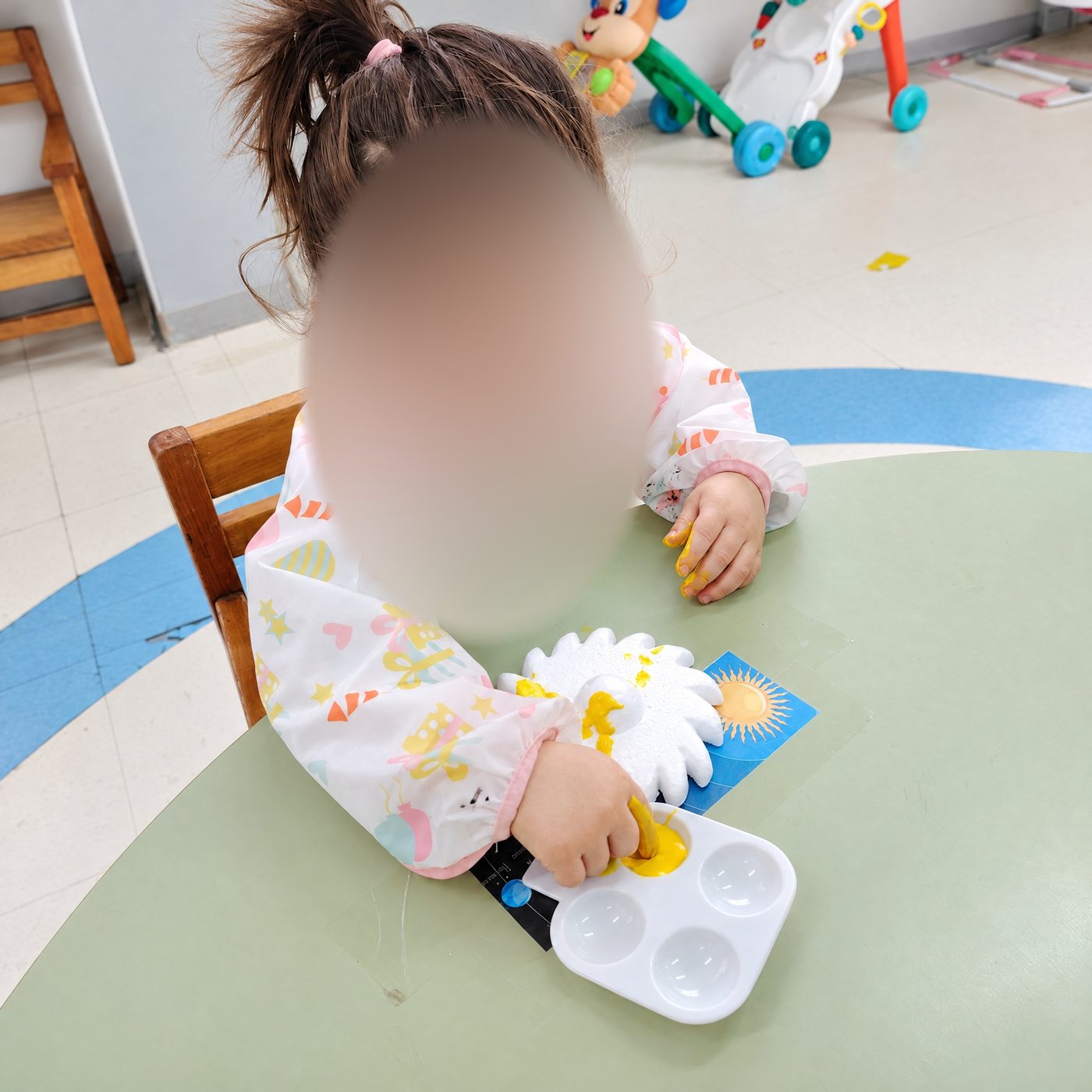 Una niña de sala cuna pinta con una esponja con forma de flor