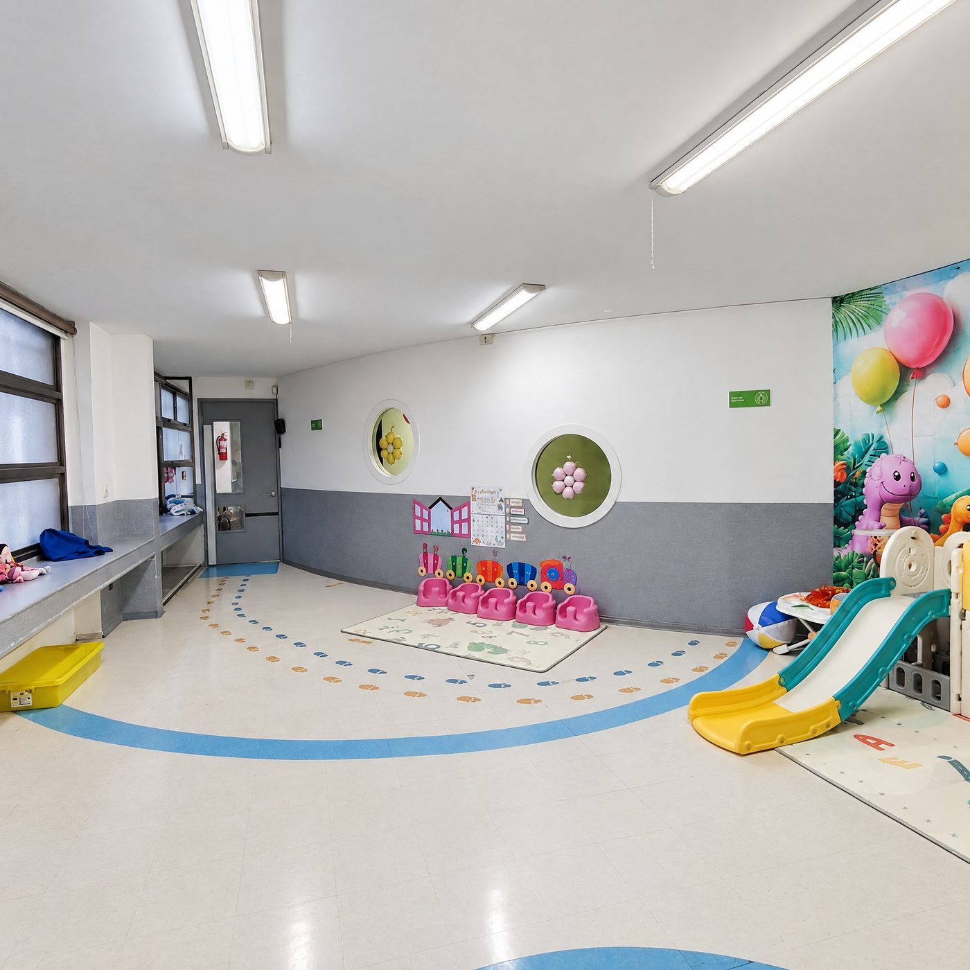 Sala de la sala cuna con colchoneta de juego, resbalín y mural de globos y dinosaurios