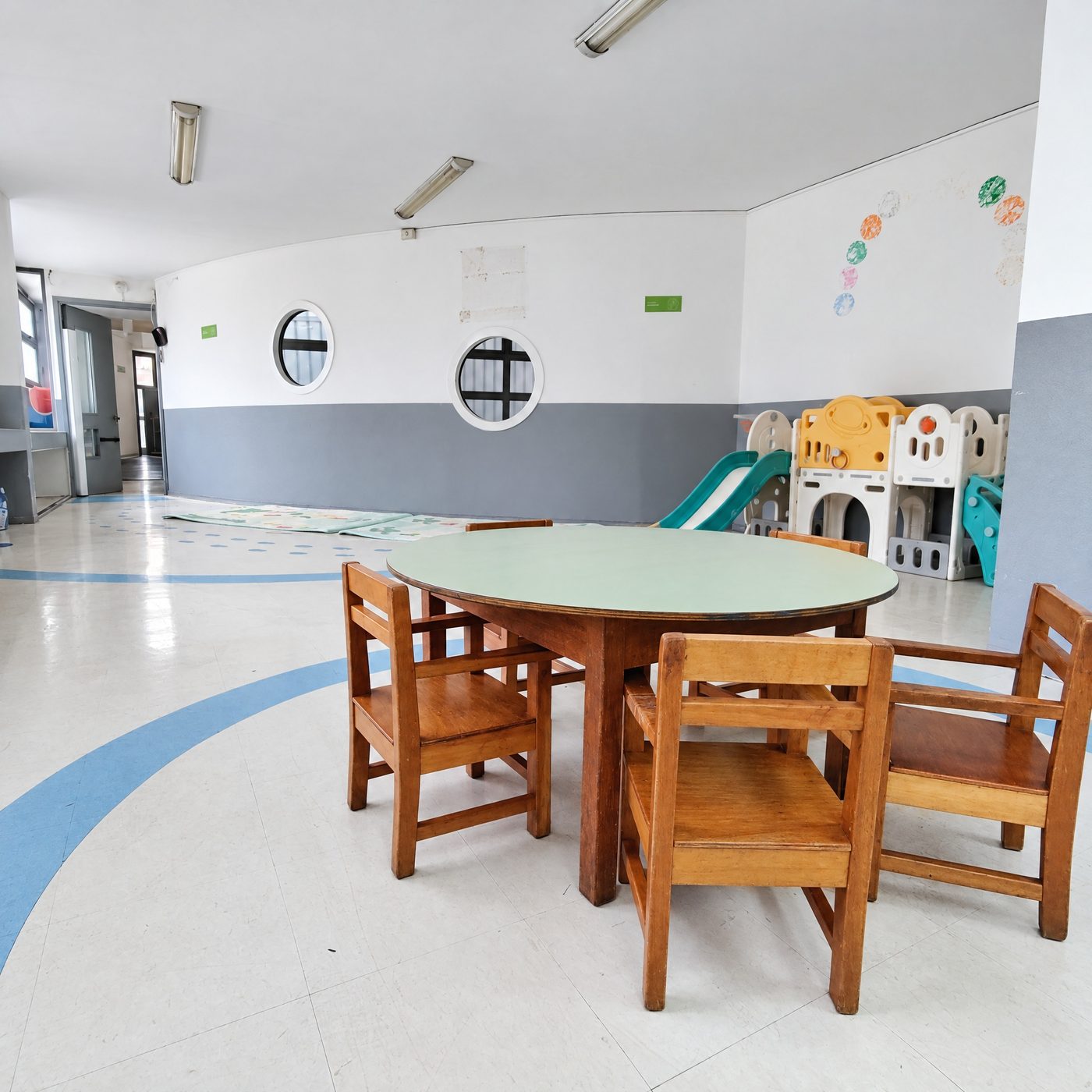 Sala de sala cuna con mesa redonda, sillas de madera y resbalín